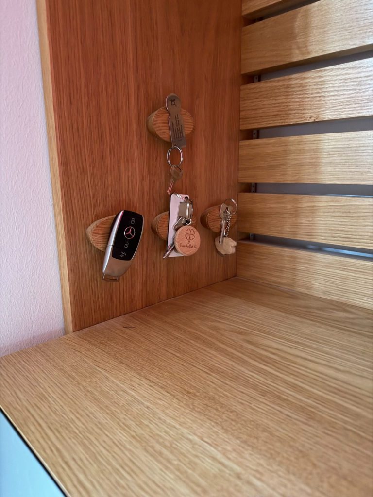 Drei Schlüsselbund mit Schlüsselanhängern an einer Holzleiste.
