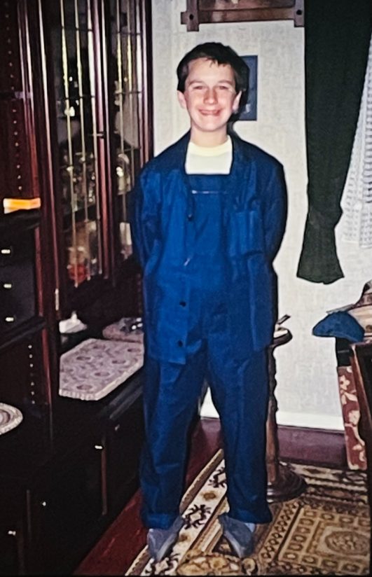 Junger Junge in blauer Latzhose steht in einem gemütlichen Raum.